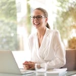 Laughing businesswoman working in office with laptop